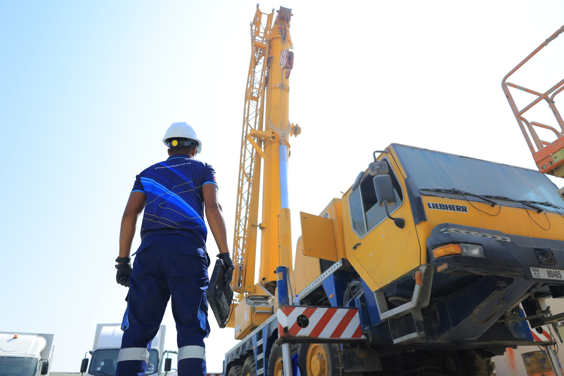 AutoDome technician with diagnostic laptop beside a Liebherr crane truck on site